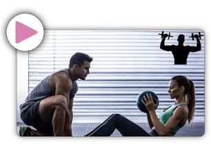 A woman in the gym with a ball in her hands supported by a trainer